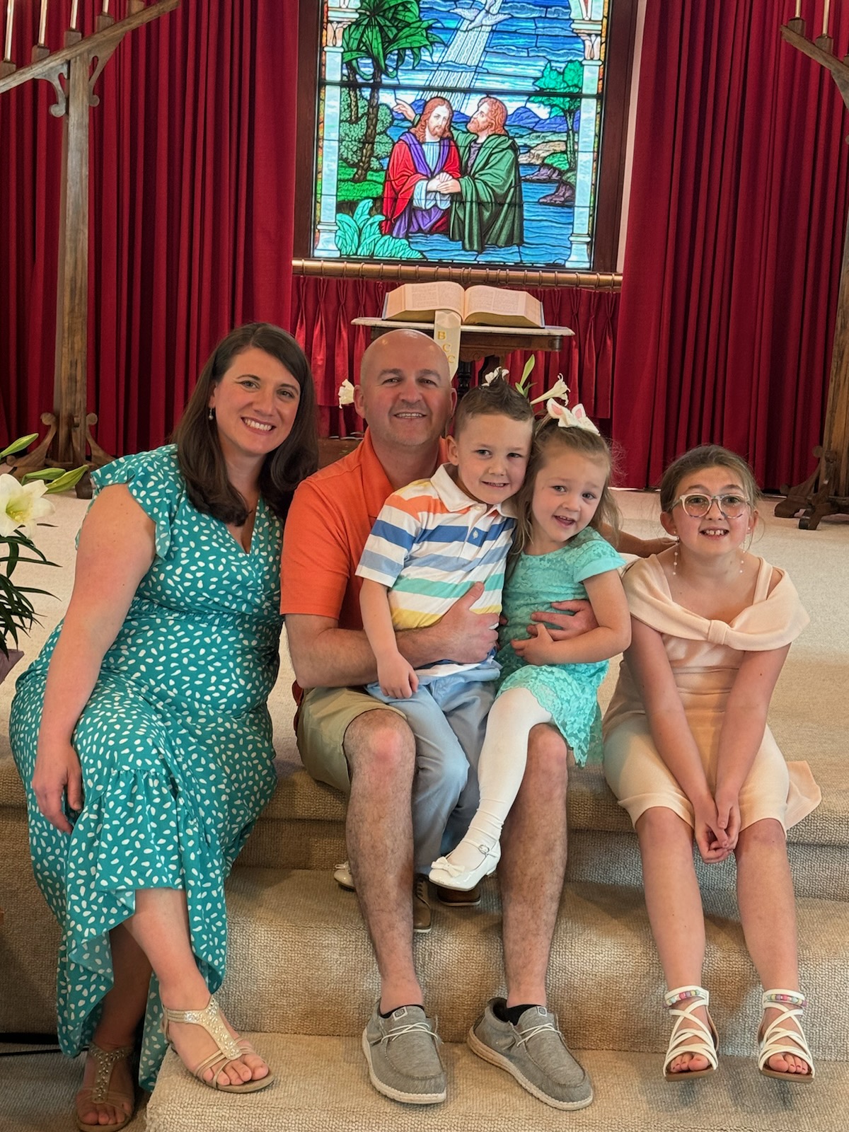 Family of 5 sitting on step in church in front of stain glass window